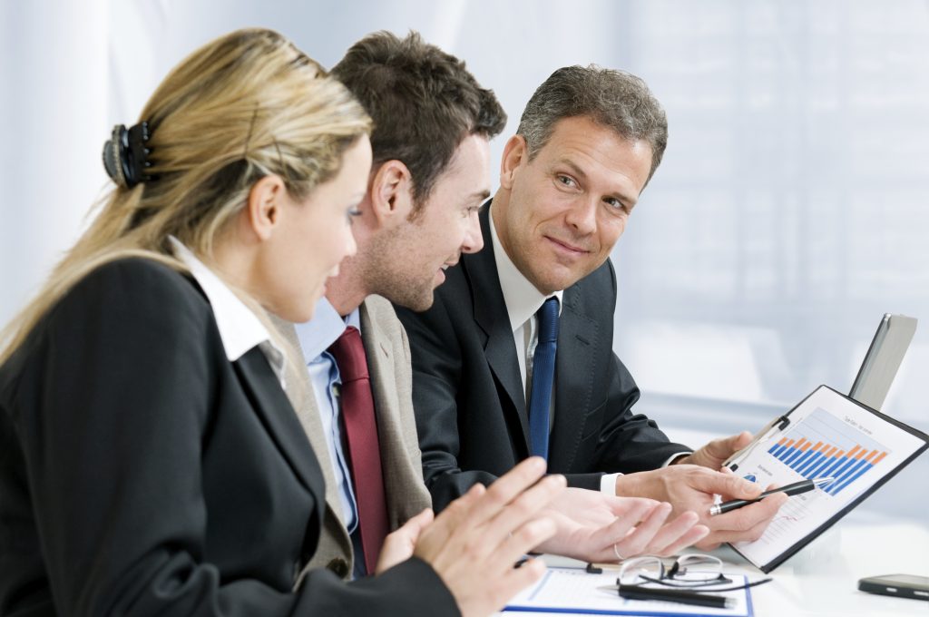 Satisfied senior businessman showing growing chart at his happy colleagues in office