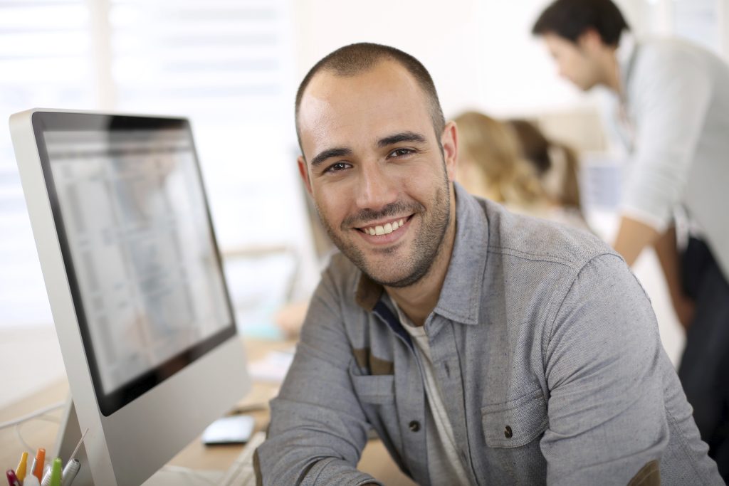 Cheerful guy sitting in front of desktop computer