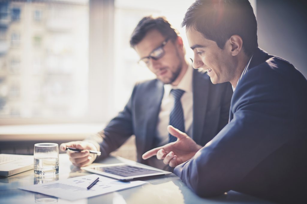 Image of two young businessmen using touchpad at meeting